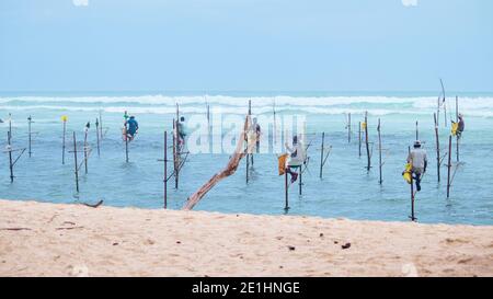 Weligama, Sri Lanka - 07 26 2020: Un gruppo di locali in un palo da palafitte, la scena di pesca nella spiaggia di Weligama, pazientemente in attesa che il piccolo pesce prenda la b Foto Stock