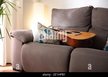 Camera con chitarra acustica su divano in un ambiente caldo Foto Stock