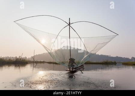 Il pescatore sulla sua barca che muove le reti oscillanti ad arco sopra il Acqua al lago Loktak Foto Stock