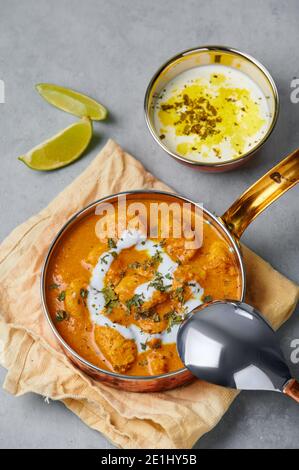 Murgh Makhani o pollo al burro in ciotola di rame su un tavolo grigio in cemento. Piatto di cucina indiana con carne di pollo e masala cremoso. Cucina asiatica e mea Foto Stock