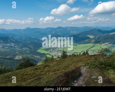 Vista sul villaggio Liptovska Luzna dal crinale dei Monti bassi Tatra con montagne, colline, prati e alberi. Slovacchia, estate soleggiato giorno, blu cielo bianco Foto Stock