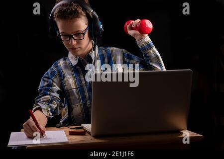 giovane studente maschile con due manubri davanti al laptop a casa scolarizzazione Foto Stock