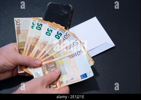 Un assegno di paga bianco è stato aperto su un tavolo nero: Le mani tengono le bollette da 50 euro, disponendole a forma di ventilatore. Immagine concettuale dello stipendio. Foto Stock