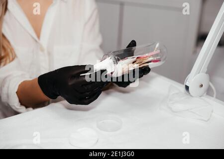Attrezzi per il trucco permanente all'interno della bottiglia nelle mani di padrone femminile in guanti neri, fuoco selettivo. Attrezzi estetician per fare il trucco delle sopracciglia. Foto Stock