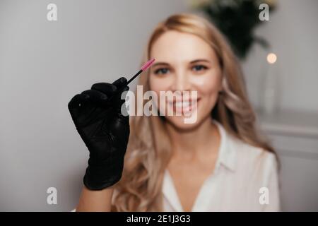 Spazzola rosa per trucco permanente nelle mani di padrone femminile in guanti neri, fuoco selettivo. Strumento estetista per fare il trucco delle sopracciglia. Cura del viso AN Foto Stock