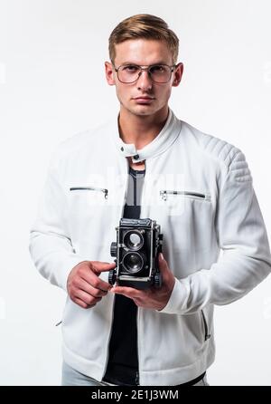 Il desiderio incontra il nuovo hobby. Bel ragazzo tenere la fotocamera retrò isolato su bianco. Il giovane fotografo indossa gli occhiali in stile casual. Attrezzature fotografiche. Hobby e stile di vita. Sessione di scatto. Foto Stock