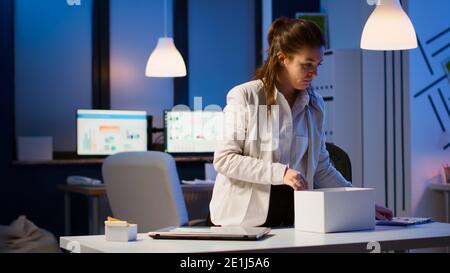 Sconvolto licenziato dipendente donna che ha messo il suo roba in scatola dal tavolo in ufficio come essere licenziato. Disoccupato che imballa le cose a tarda notte. Donna che chiude il laptop e lascia l'ufficio del posto di lavoro a mezzanotte Foto Stock