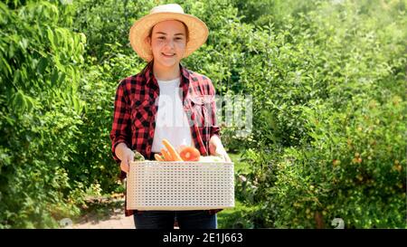 Ritratto di felice agricoltore sorridente che cammina in giardino e tenendo scatola con verdure biologiche mature. Concetto di piccola impresa e di crescita organica Foto Stock