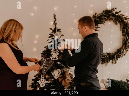 Famiglia con moglie incinta decora la casa per il nuovo anno. Mattina di Natale. Interno. Festa di San Valentino Foto Stock