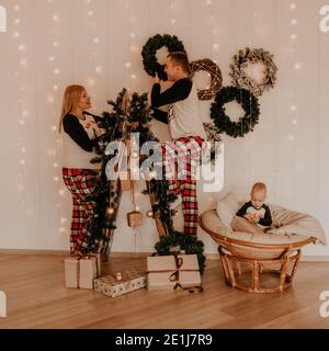 La famiglia con la moglie incinta sulla scala decora la casa per la bambina di nuovo anno che si siede in una sedia e gioca. Mattina di Natale. Nuova Y Foto Stock