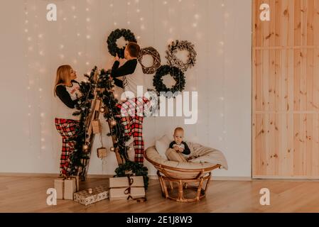 La famiglia con la moglie incinta sulla scala decora la casa per la bambina di nuovo anno che si siede in una sedia e gioca. Mattina di Natale. Nuova Y Foto Stock