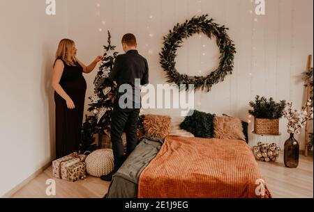 Famiglia con moglie incinta decora la casa per il nuovo anno. Mattina di Natale. Interno. Festa di San Valentino Foto Stock