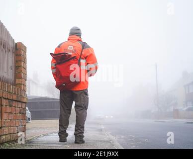 Kidderminster, Regno Unito. 7 gennaio 2021. Tempo in Gran Bretagna: Nebbia pesante e temperature di congelamento sono lenti a salire a Kidderminster. Questo postino cammina con attenzione lungo una strada residenziale nebbiosa, tutte le strade laterali sono ancora ghiacciate e marciapiedi molto scivoloso sotto il piede. Credit: Lee Hudson/Alamy Live News Foto Stock