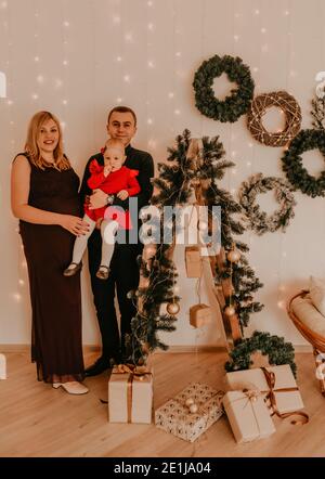 La famiglia felice con la moglie incinta sulla scala decora la casa per il nuovo anno. Mattina di Natale. Interno. Festa di San Valentino Foto Stock