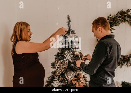 Famiglia con moglie incinta decora la casa per il nuovo anno. Mattina di Natale. Interno. Festa di San Valentino Foto Stock