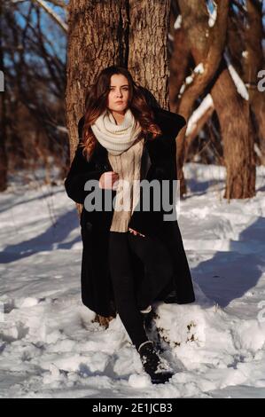 Ragazza appoggiata sull'albero nella foresta d'inverno. Giornata invernale soleggiata Foto Stock