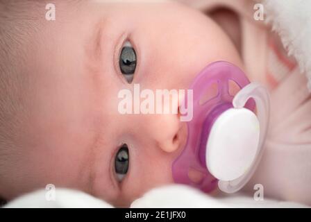 Il neonato è appoggiato su un lato con un succhietto bianco in bocca Foto Stock