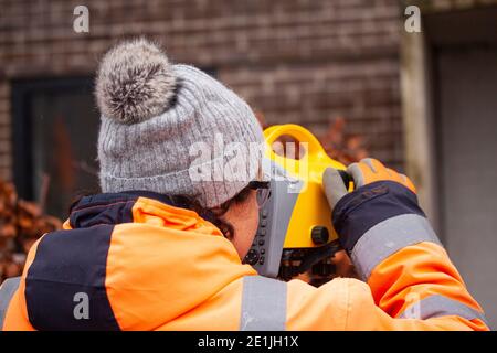 Topografia terrestre femminile che utilizza un livello di misurazione digitale di precisione a. stabilire o verificare o misurare l'altezza dei punti specificati relativo a una da Foto Stock