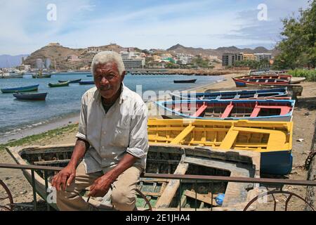 Un vecchio pescatore si trova sul bordo di una recinzione di ferro sulla spiaggia di Mindelo, Capo Verde. Foto Stock