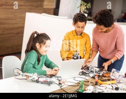 Smily African American insegnante di scienza femminile con gruppo di bambini programmazione di giocattoli e robot elettrici in classe robotica Foto Stock