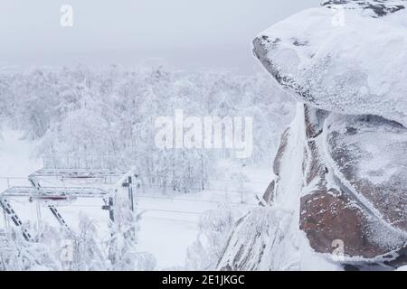 roccia ghiacciata sullo sfondo dell'ultima torre di lo skilift su una collina innevata tra alberi gelidi Foto Stock