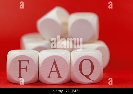 Tre cubetti di legno con le lettere F A Q contro uno sfondo rosso Foto Stock