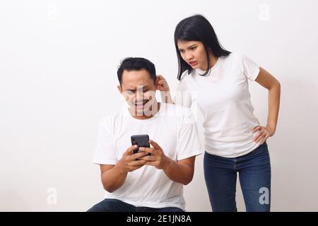 Arrabbiato giovane donna che tira lobo dell'orecchio sorpreso scioccato nel dolore che colpisce l'uomo divertente. Cute ragazza che mostra tira l'orecchio dopo aver guardato uno smartphone del ragazzo Foto Stock