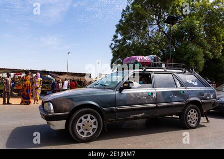 MBOUR, SENEGAL - CIRCA GENNAIO 2021. Un uomo nero maturo che guida in un'auto molto vecchia nera indossando maschera di protezione contro la pandemia del coronavirus, Foto Stock