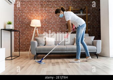 Donna pulizia del pavimento in legno duro con mop in maschera facciale Foto Stock