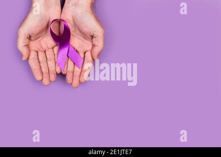 Mani dell'uomo che tengono un nastro viola su uno sfondo viola Foto Stock