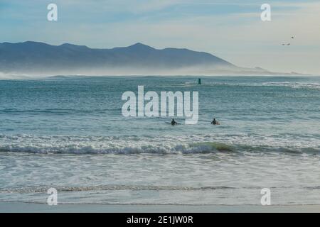 Idilliaco mare. Oceano tranquillo, montagne e silhouette surfisti a Morro Bay, California Foto Stock
