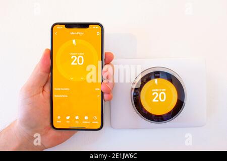 Calgary, Alberta, Canada. Jan 03 2021. Una persona che tiene un iPhone 11 Pro Max accanto a un termostato intelligente Nest mentre il calore è acceso. Foto Stock
