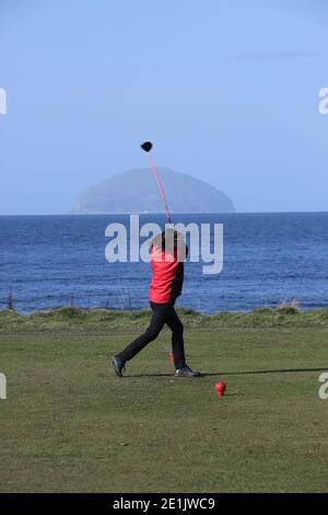 Campo da golf municipale di Girvan, Ayrshire, Scozia, Regno Unito. Donna golfista sul primo tee con Ailsa Craig in terra posteriore Foto Stock