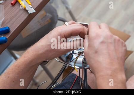 un uomo fa il cablaggio su un lampadario per appendere dal soffitto in un appartamento. Miglioramento e riparazione dei locali. Foto Stock