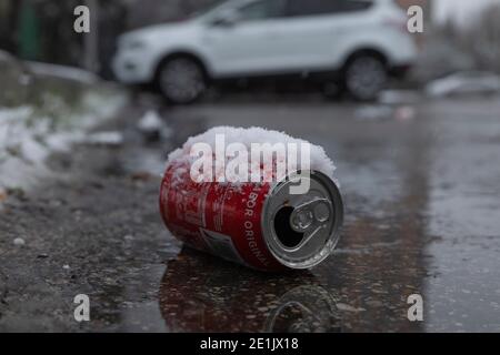 Madrid, Spagna - 07 gennaio 2021: Una lattina rossa di Coca Cola, ricoperta di neve, gettata sulla strada, sporca e inquinante l'ambiente urbano. Foto Stock