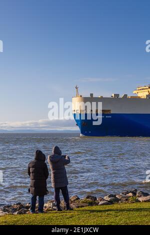 Due giovani donne che fotografano l'arrivo di una grande nave di trasporto di veicoli nell'estuario del fiume Fraser sulla rotta dall'Asia, Steveston British Columbia Foto Stock