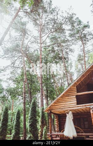 L'abito da sposa pende sul muro di legno nella foresta Foto Stock