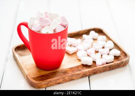 Tazza rossa di cacao caldo con marshmallows a forma di cuore sfondo bianco di legno Foto Stock