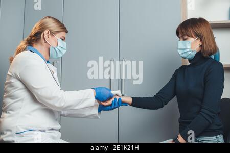 Il medico biondo senior sta misurando la temperatura sulla mano del paziente utilizzo di un termometro elettrico in ufficio Foto Stock