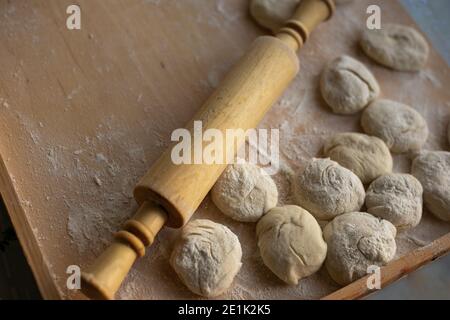 preparare l'impasto per la cottura, arrotolare l'impasto di lievito, gli sbozzati per torte e un mattarello si trovano su una tavola di legno, spazio per la copia Foto Stock