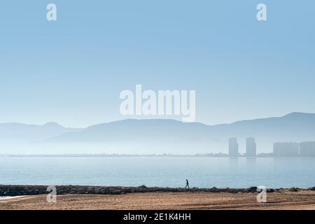 Spiaggia di sabbia vuota e silhouette dello skyline di Cullera. Mediterraneo Seape, cielo nuvoloso e nebby nebbia paesaggio urbano vista distante. Provincia Foto Stock