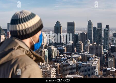 Montreal, CA - 6 Gennaio 2021 : uomo che indossa una maschera in mezzo all'epidemia di coronavirus guardando lo skyline di Montreal dalla cima del Monte Royal Foto Stock