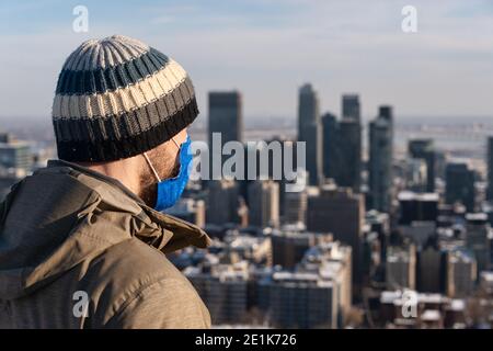 Montreal, CA - 6 Gennaio 2021 : uomo che indossa una maschera in mezzo all'epidemia di coronavirus guardando lo skyline di Montreal dalla cima del Monte Royal Foto Stock