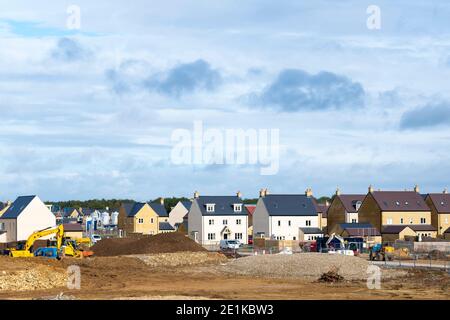 Costruttori che lavorano con JCB digger su un nuovo sviluppo di alloggi a West Witney alla periferia di Oxford, West Oxfordshire, Inghilterra a causa della popolazione g. Foto Stock