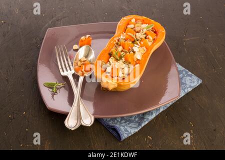 Butternut cotta a metà presentata su un piatto con posate vecchie su sfondo nero Foto Stock