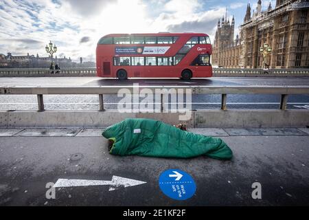 Un sonno sconnesso nel suo sacco a pelo a mezzogiorno su Westminster Bridge, Londra, Regno Unito. Foto Stock