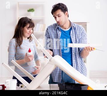 La moglie aiutando il marito per riparare sedia rotta a casa Foto Stock