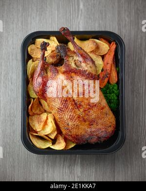 anatra e verdure appena tostate in contenitore di plastica pronto per la consegna su tavolo da cucina in legno grigio, vista dall'alto Foto Stock