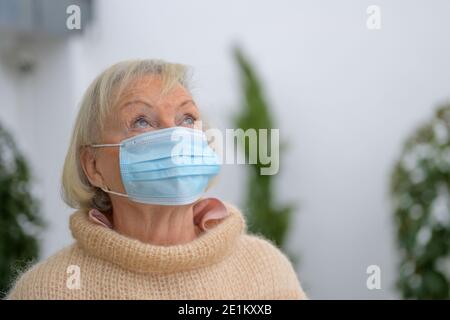 Nonna anziana che indossa una maschera protettiva durante il Covid-19 pandemia in piedi all'aperto guardando in su con un'espressione premurosa con copyspa Foto Stock