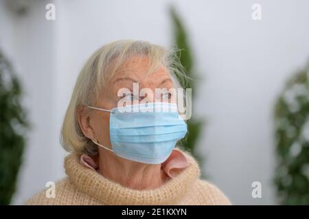 Donna anziana dagli occhi blu che indossa una maschera facciale come protezione durante La pandemia di Covid-19 in piedi all'aperto guardando in su con un attento espressione in a. Foto Stock